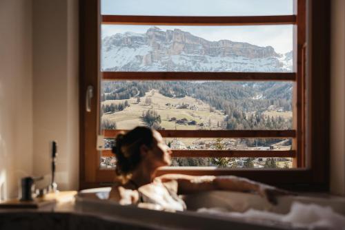 a woman in a bath tub with a mountain view at Hotel Melodia del Bosco in Badia