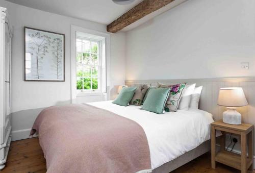 biała sypialnia z dużym łóżkiem z zielonymi poduszkami w obiekcie A beautiful Cotswolds Cottage in Stroud w mieście Stroud