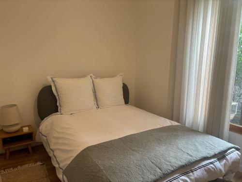 - un lit avec des draps et des oreillers blancs à côté d'une fenêtre dans l'établissement JO : Charmant appart proche de Paris, à LʼÎle-Saint-Denis