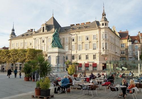 a large building with people sitting at tables in front of it at Cityhotel am Domplatz Self-CheckIn in Klagenfurt
