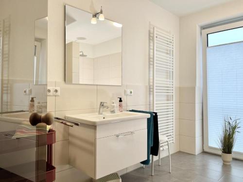 ein weißes Badezimmer mit einem Waschbecken und einem Spiegel in der Unterkunft Quartier Hohe Geest 19 in Cuxhaven