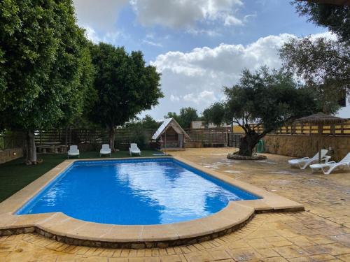 a large blue swimming pool with chairs and trees at Casa Rural El Almendrillo in Arcos de la Frontera