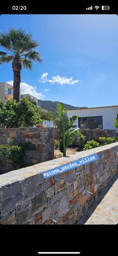 a stone wall with a palm tree in front of a building at Gioma Garden Villas in Istron