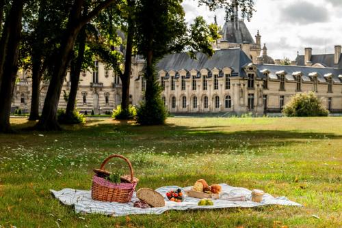 a picnic with bread and a basket on a blanket in front of a building at Auberge du Jeu de Paume in Chantilly