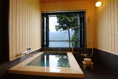 a bathroom with a bath tub with a window at Rakuyu in Fujikawaguchiko