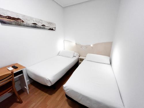 a room with two beds and a desk and a table at Pensión Régil in Donostia-San Sebastián