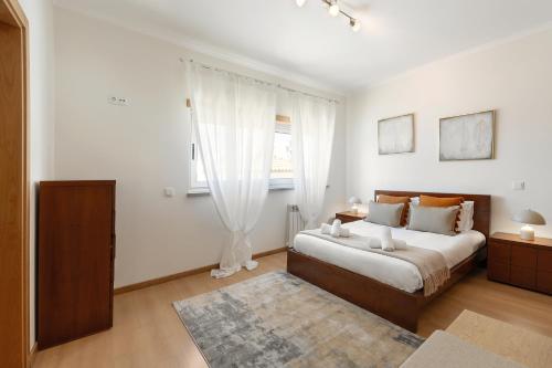 a white bedroom with a bed and a window at Nazaré Beach House in Nazaré
