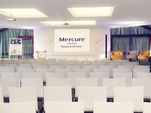 une salle de conférence vide avec des chaises blanches et un écran dans l'établissement Mercure Caen Cote De Nacre, à Caen