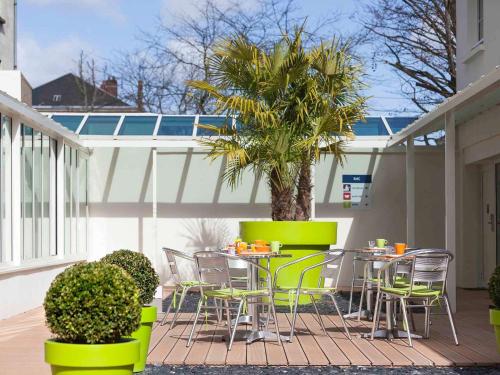a patio with chairs and a table and a palm tree at ibis Styles Saumur Gare Centre in Saumur