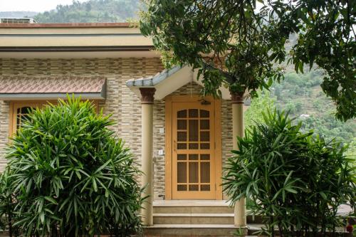 a house with a yellow door and two trees at The Mountain Retreat, Muzaffarabad in Muzaffarabad