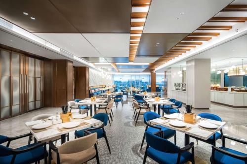 a restaurant with white tables and blue chairs at Hilton Garden Inn Huzhou High-Speed Railway Station in Huzhou