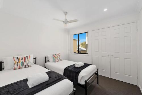 a white bedroom with two beds and a window at Jetty Escape Townhouse in Coffs Harbour