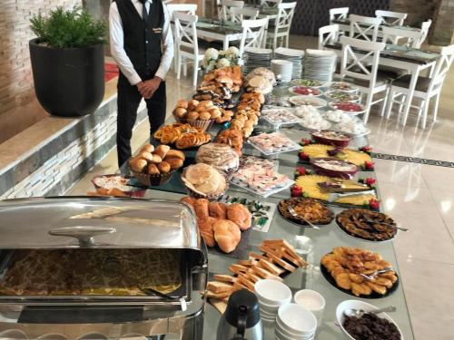 a table of food with a man standing in front of it at Grand Plaza Hotel & Resort in Qaryat ash Shamālī