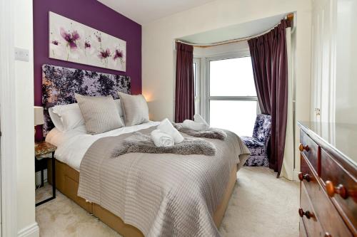 1 dormitorio con 1 cama con paredes de color púrpura y ventana en Beautiful family home in Mumbles, with garden en The Mumbles