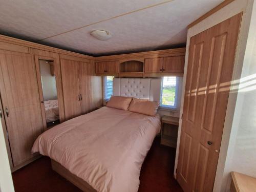 uma cama num pequeno quarto com armários de madeira em Great Caravan With Spacious Decking Southview Holiday Park, Skegness Ref 33035v em Skegness