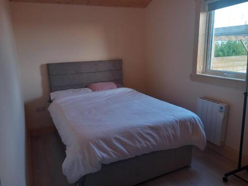 a bedroom with a bed with white sheets and a window at Kilcavan Chalet in Gorey