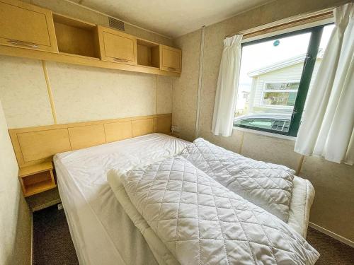 ein kleines Bett in einem kleinen Zimmer mit Fenster in der Unterkunft 8 Berth Caravan With Free Wifi At Heacham Holiday Park In Norfolk Ref 21008e in Heacham