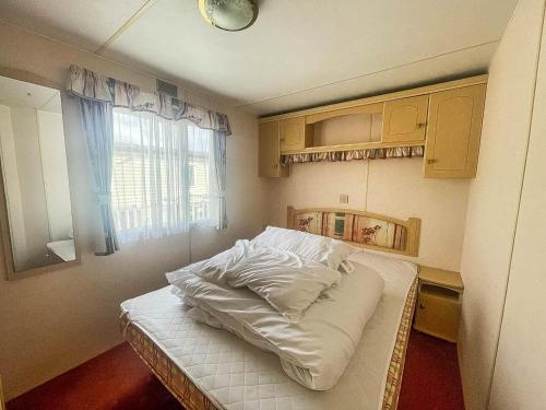 a small bed in a room with a window at 6 Berth Caravan With Decking Nearby Heacham Beach In Norfolk Ref 21047a in Heacham