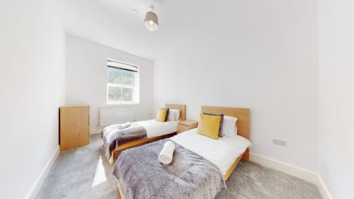 twee bedden in een kamer met witte muren en een raam bij Spacious three bedroom apartment with Valley views in Abertillery