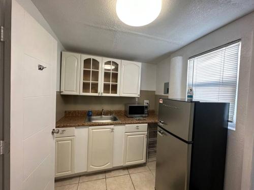 uma cozinha com armários brancos e um frigorífico preto em Miami Breeze Studio em Miami Gardens