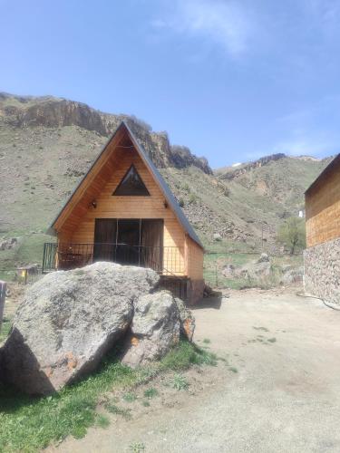 una cabaña de madera con una gran roca delante de ella en Gold Star en Kazbegi