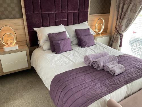 um quarto com uma cama grande com lençóis e almofadas roxos em Tattershall VIP Lodge- Lakeside setting with hot tub and private fishing peg situated on Osprey lake tattershall park em Tattershall