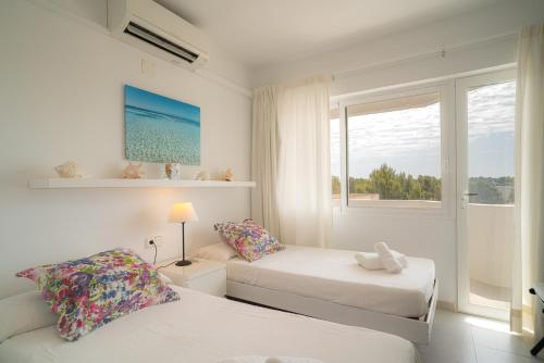 a white bedroom with two beds and a window at Mirada I in Es Pujols