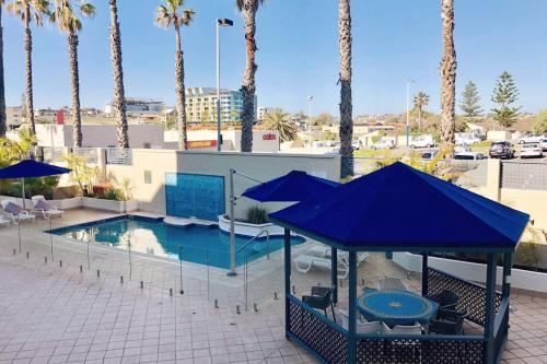 a pool with blue umbrellas and chairs next to a building at Sandcastles At The Beach Outstanding Location! in Perth