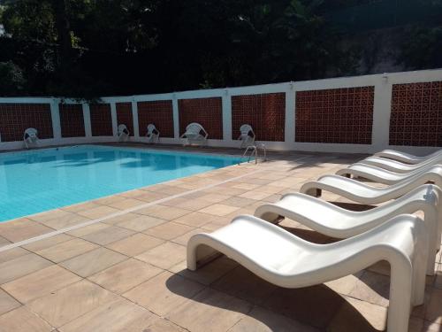 a row of white chairs next to a swimming pool at Apartamento Parque Jardim Europa in Rio de Janeiro