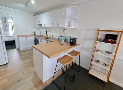 Chic 2 Bed Apartment On Scarborough Beach في بيرث: مطبخ مع دواليب بيضاء وكاونتر مع الكراسي