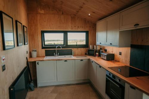 a kitchen with white cabinets and a sink and a window at Dome Meadow 1 with Outdoor Tub At Tapnell Farm in Yarmouth