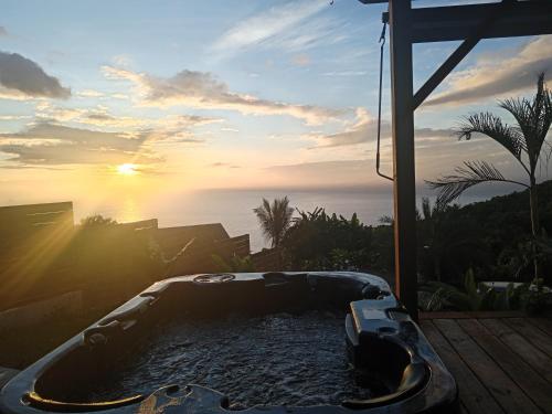 een hot tub op een patio met de zonsondergang op de achtergrond bij Bungalow de luxe en bois avec Spa in La Possession