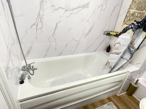 uma banheira branca na casa de banho com paredes em mármore em Westfield Gardens Apartment - 3 bedrooms em Goodmayes