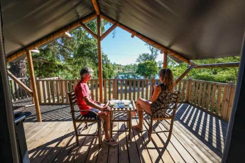Un ragazzo e una ragazza seduti a un tavolo su un ponte di Les Auzerals camping du lac a Rabastens