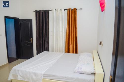1 dormitorio con cama blanca y cortina naranja en La bonté, en Abomey-Calavi