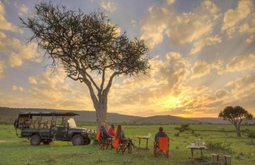 eine Gruppe von Menschen, die an Tischen unter einem Baum sitzen in der Unterkunft Orwas maasai Mara safari camp in Kenya in Sekenani