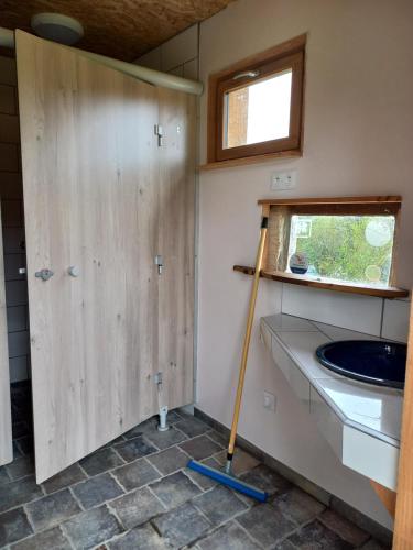a bathroom with a sink and a wooden door at Tiny House et yourte sous les Poiriers in Domfront