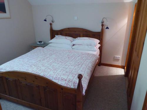a bedroom with a wooden bed with white sheets and pillows at Craigruie Farmhouse in Balquhidder