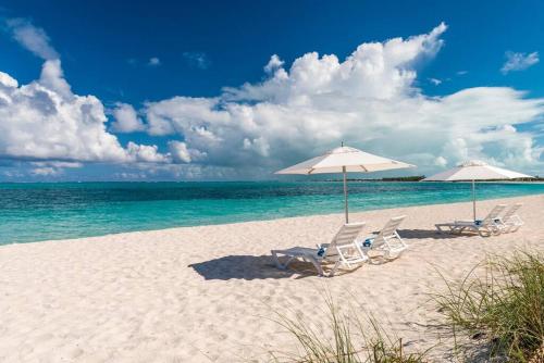 two chairs and umbrellas on a beach with the ocean at Casa Grande - Grace Bay Beach in The Bight Settlements