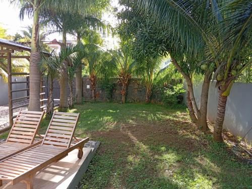 2 chaises en bois assises dans une cour avec des palmiers dans l'établissement Villa Coco, à Trou aux Biches