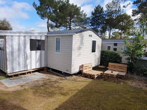 a white tiny house with two benches and benches at Camping du Bois Dormant in Saint-Jean-de-Monts