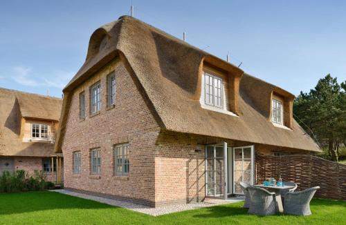 a house with a thatched roof with a table in front at Hotel Duene in Rantum