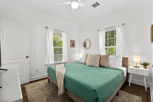a white bedroom with a bed and two windows at Treetop Cottage - 3 blocks from Historic District in St. Augustine