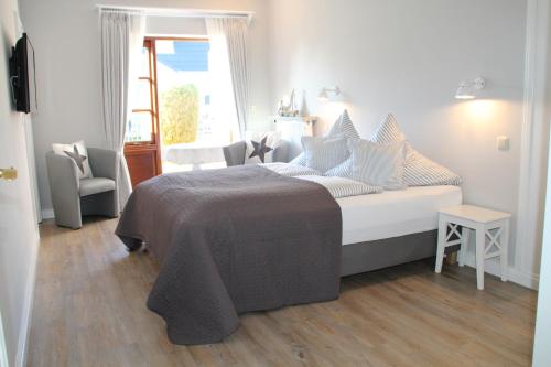 a white bedroom with a bed and a window at Landhaus Nordstern Hotel garni in Utersum