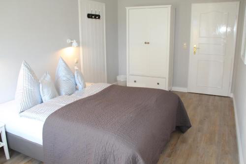 a white bedroom with a large bed with blue pillows at Landhaus Nordstern Hotel garni in Utersum