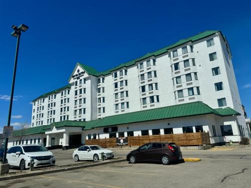 a large white building with cars parked in a parking lot at Divya Sutra Plaza and Conference Centre Calgary Airport in Calgary