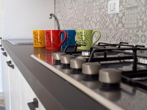 three colorful coffee mugs sitting on top of a stove at Kalimera Apartment in Santo Stefano di Camastra