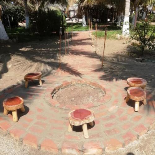 a fire pit with three wooden benches in a park at Punta Pacífico Bungalows Máncora in Máncora