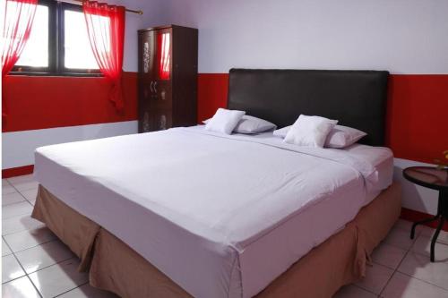 OYO 93168 Permata Ria Hotel في مانادو: سرير كبير في غرفة بجدار احمر