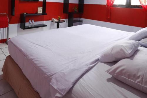 Una gran cama blanca en una habitación con una pared roja. en OYO 93168 Permata Ria Hotel en Manado